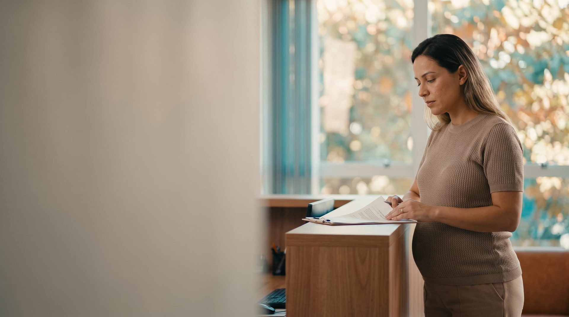 Mulher grávida trabalhando na recepção de um escritório, sob luz natural.